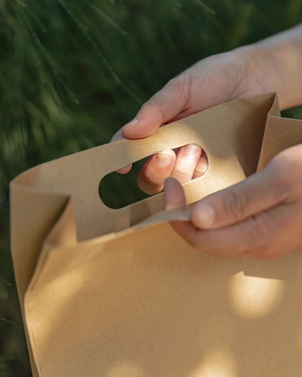 Mains tenant un sac en papier kraft devant un feuillage